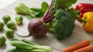 Vue rapprochée de légumes frais variés sur une table en bois clair. Inclut betterave, brocoli, choux de Bruxelles et bok choy.